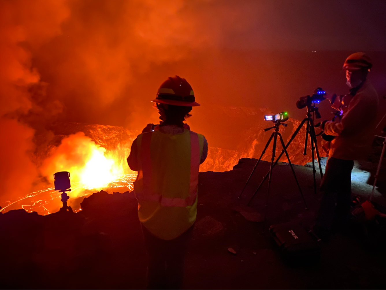 Nighttime photo of scientists collecting data during a volcanic eruption, backlit by lava