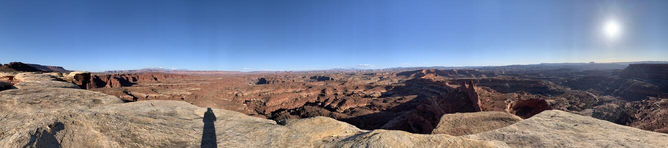 A person's shadow is displayed on the rock as they look out over a panorama of Canyonlands National Park