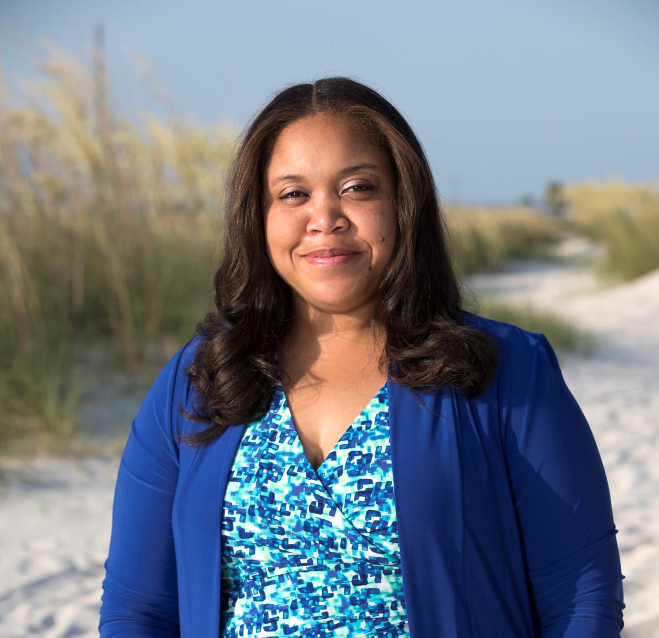 a woman in a blue jacket stands on a vegetated sandy beach