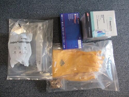 Bags containing safety goggles and yellow gloves, and boxes of face masks.