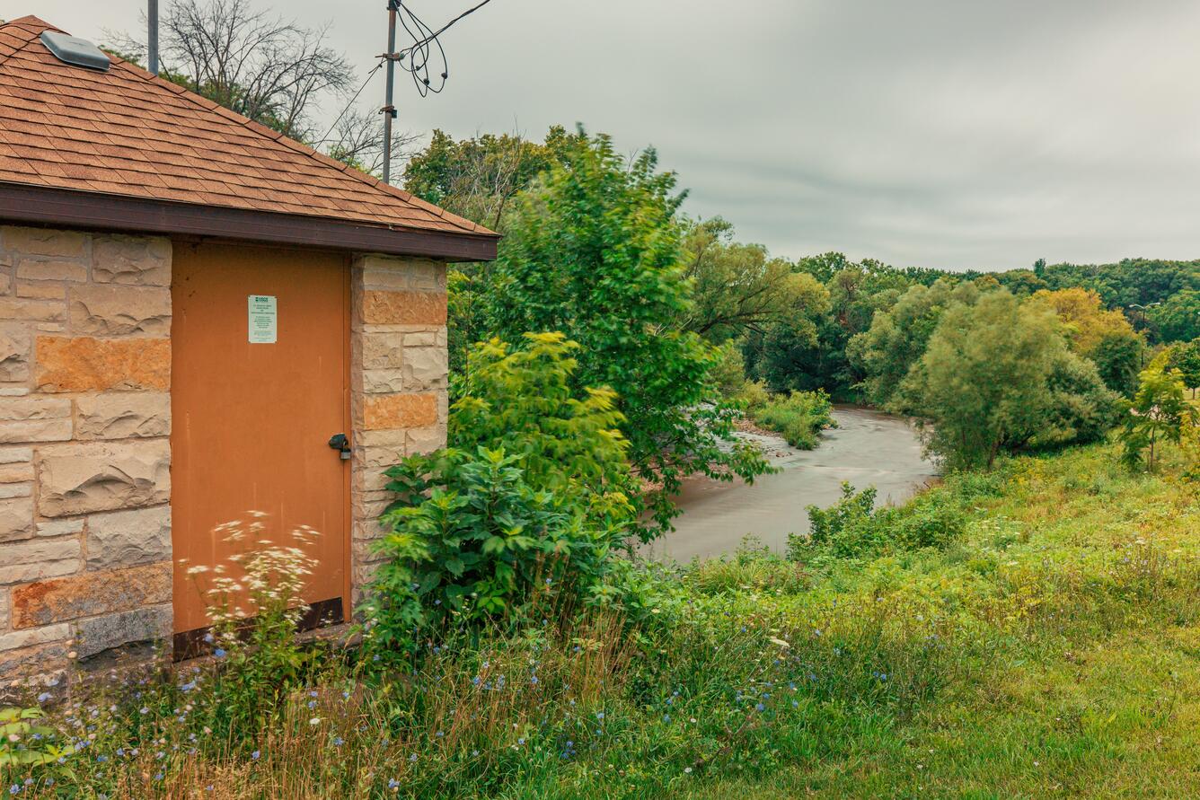 Streamgage house in front of river with green foliage