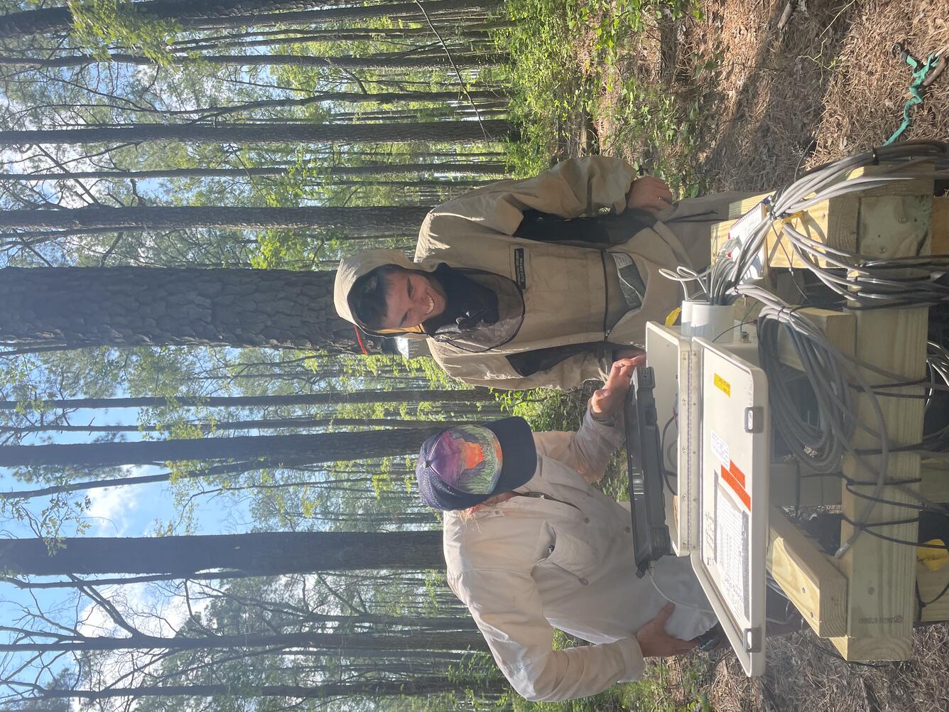 Two scientists look down at a tablet that is connected to a monitoring box in the middle of a forest at Money Stump marsh
