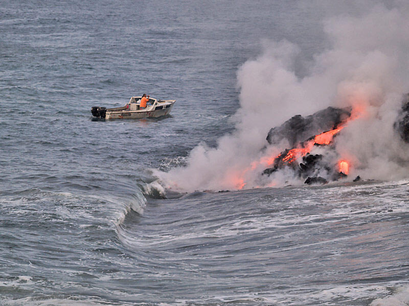 This is a photo of a lone boatsman videoing a lava entry at end of western lava delta.