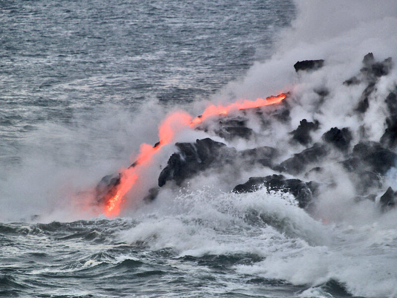 This is a photo of a single lava stream emerging from a small tube and coursing down to water.