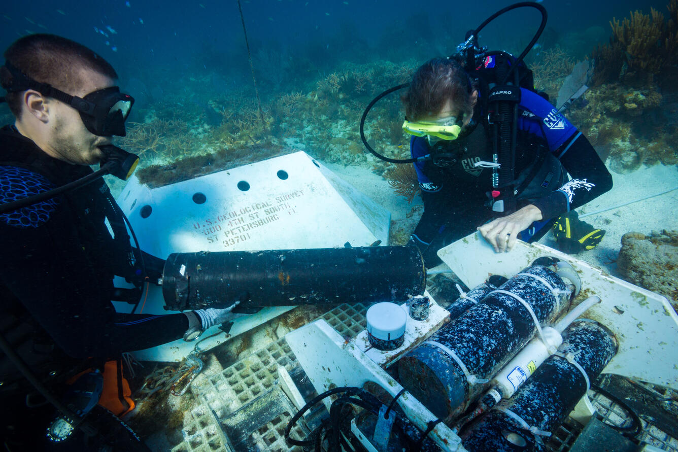 Two scuba divers handling a large piece of scientific equipment at the bottom of the ocean