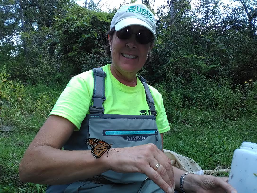 woman with USGS clothing in green woodsy area with orange butterfly on arm