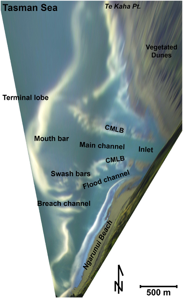 Overhead view of coast with green land on right, blue water plus bands of white on left. Sand bars and other features labeled.