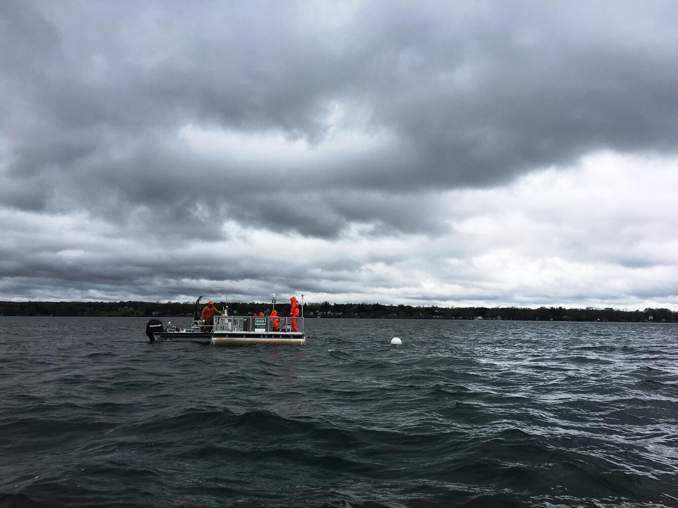 storm clouds over USGS floating HABS platform and boat  with USGS staffers on choppy lake waters