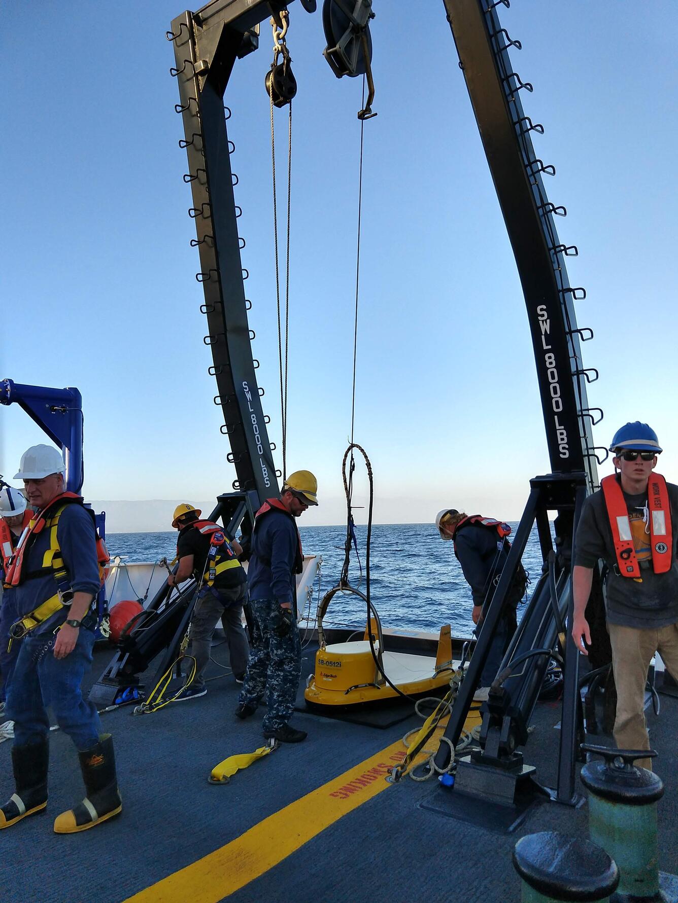 A group stands on the stern of a ship preparing an instrument attached to a cabling system.