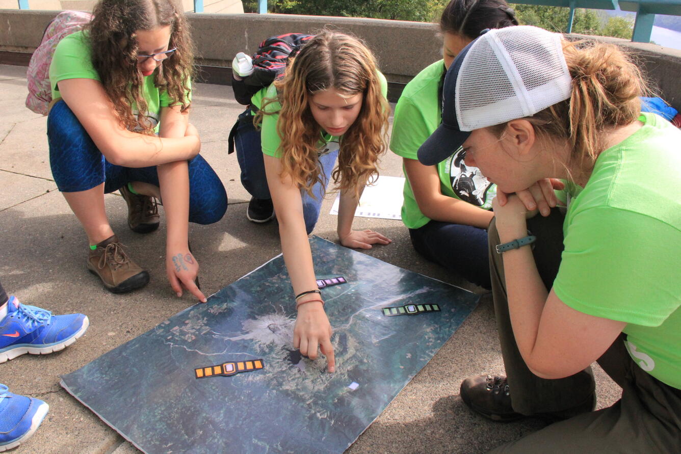 Girls points to a location on a map laying on the ground.