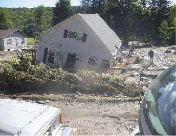 house tilted sideways and debris from flood