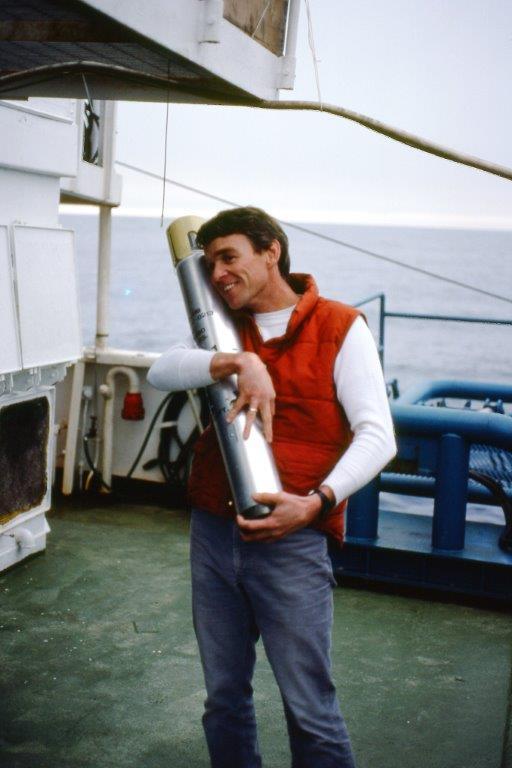 A man standing on the deck of a ship holds a core sample taken from the ocean floor.