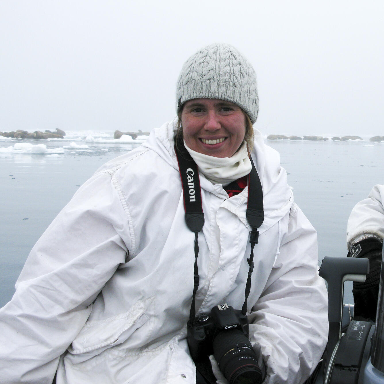 Sarah Sonsthagen in a boat with a camera around her neck.  She is in the Chukchi Sea doing walrus research