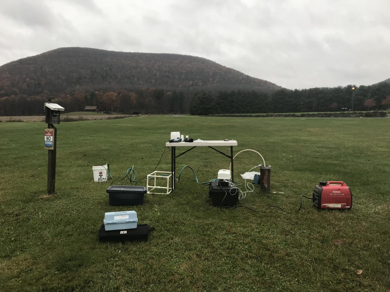 Gray skies. A park-like expanse of lawn with a hill in the background. A well and water-quality sampling equipment.