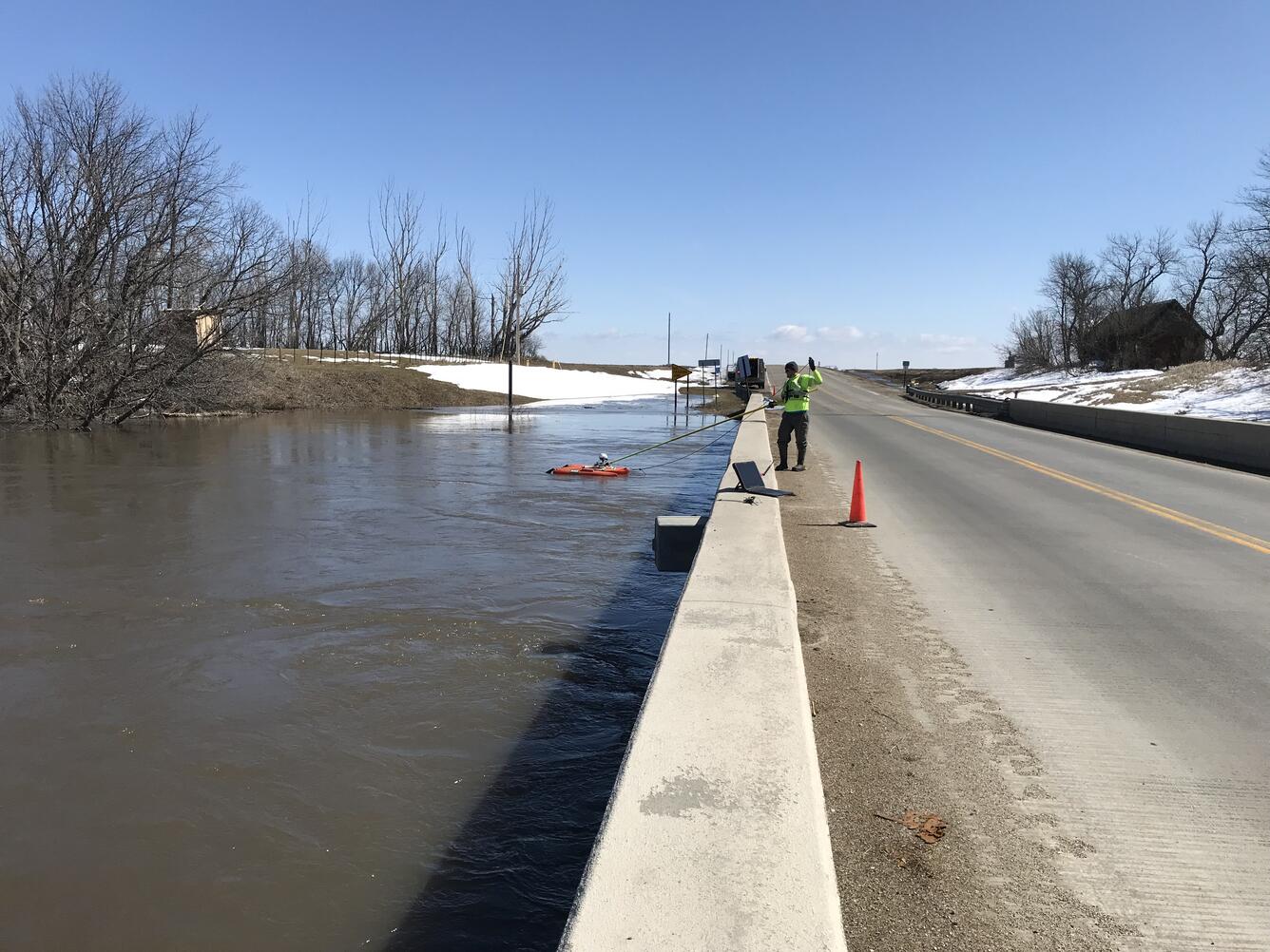 USGS Technician taking a water measurement from a bridge of floodwaters below