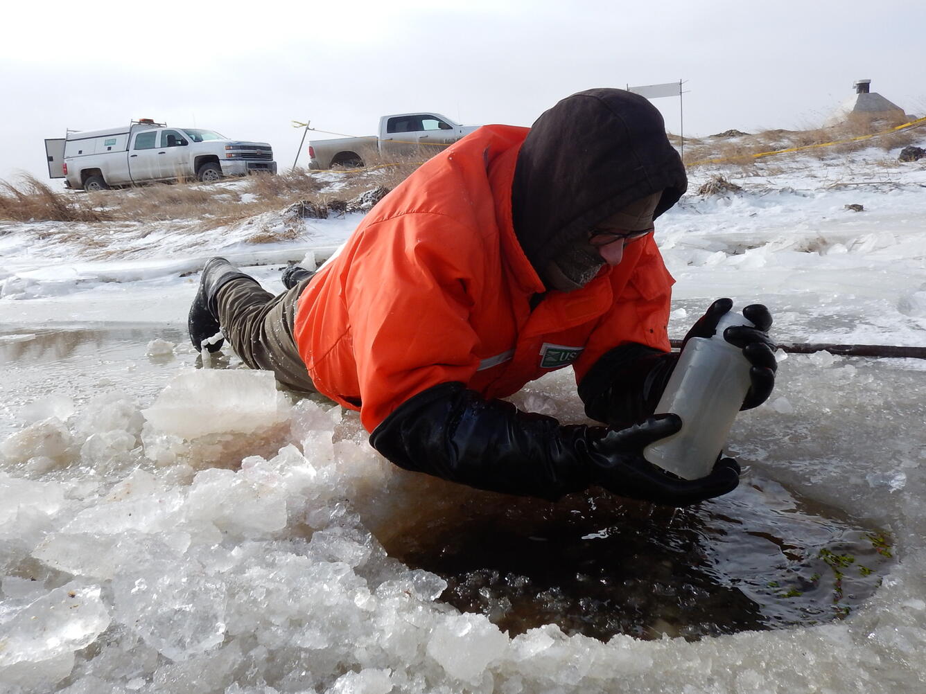 USGS scientist lifting a sample bottle from ice hole 