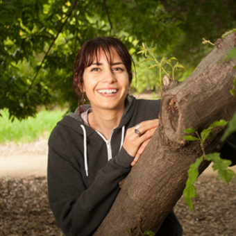 Headshot of Nina Fontana wearing a black zip up sweater and leaning up against a tree branch.