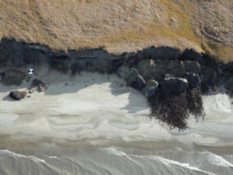 View from above looking back at a coastal bluff where large sections have collapsed and crumbled onto the beach.
