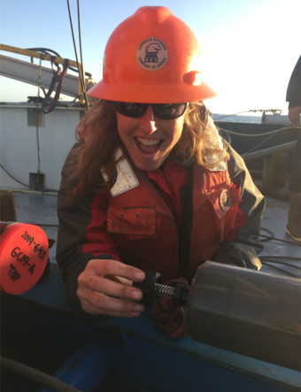 A smiling woman holds a spring-loaded instrument against a sediment core.