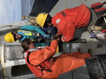 People work on the deck of a ship securing a long coring device.